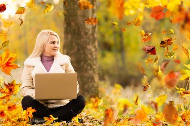 a young woman in a red sweater sits under an oak tree in an autumn forest on a sunny day, a bouquet of yellow maple leaves in her hands, autumn mood, I love autumn. High quality photo