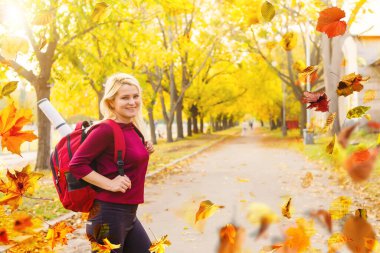 Beautiful girl walking outdoors in autumn. Smiling girl collects yellow leaves in autumn. Young woman enjoying autumn weather. High quality photo