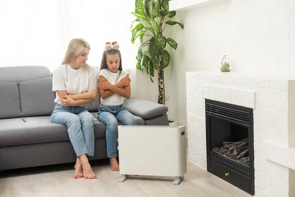 Cold home, freezing family, mother and daughter Sitting Near Heater.