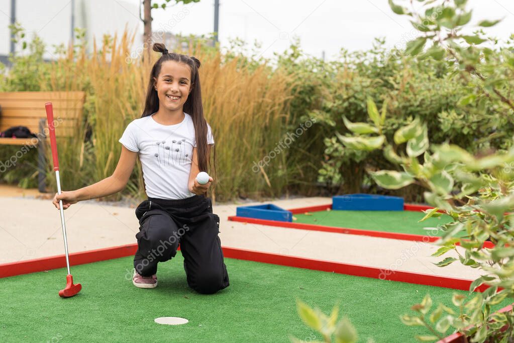 Cute preschool girl playing mini golf with family. Happy toddler child having fun with outdoor activity. Summer sport for children and adults, outdoors. Family vacations or resort.