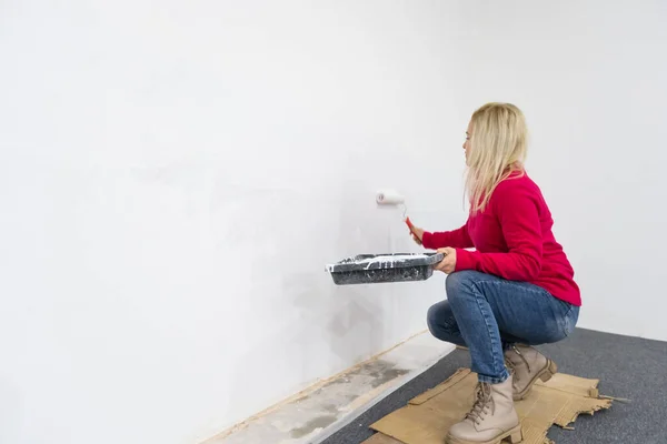 the woman painting walls with roller equipment while moving in apartment. Renovating new house and improvement concept.