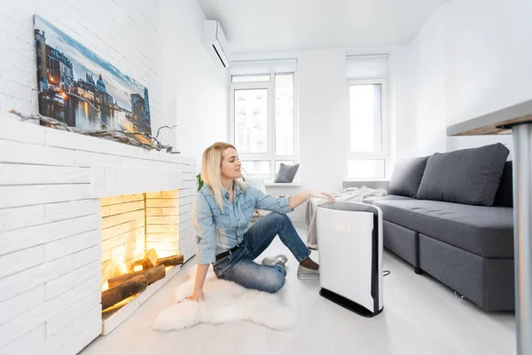 Woman relaxing at home with working air humidifier on the foreground. Concept of home air humidification.