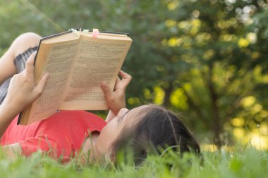 Bahçede kitabı olan küçük bir kız. Çocuk elinde bir kitap okuyor. Yazın açık havada. Kırsal.