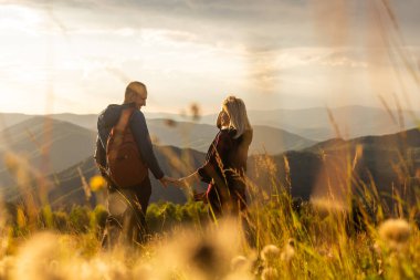 Erkek ve kadın dağın tepesinde ayakta ve sarılıyor, sonbahar yürüyüşü sırt çantalarıyla.