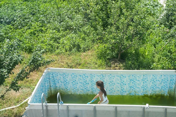 a little girl cleans a very dirty pool.