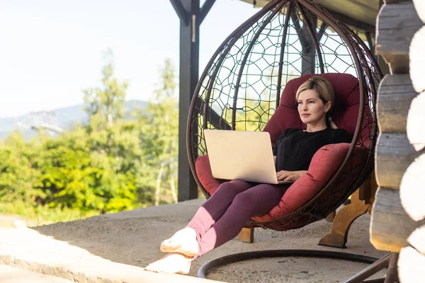 Dışarıda bilgisayar başında çalışan dağ manzaralı bir kadın.