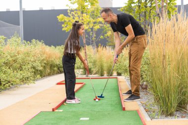 father and daughter playing mini golf together in the park.