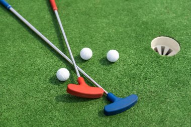 Assorted miniature golf putters and balls askew on synthetic grass