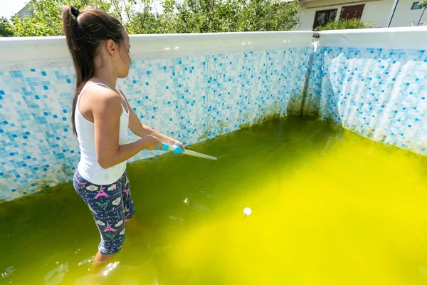 a little girl cleans a very dirty pool.