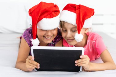 Noel, Noel, Noel, kış, mutluluk konsepti - tabletle oynayan iki sevimli kıvırcık kız.
