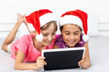 Heyecanlı küçük kardeş çocuklar modern tablet aletleriyle oynarken eğleniyorlar. Mutlu küçük kız çocukları ped cihazıyla video izleyip, kış tatillerinde evde eğleniyorlar.