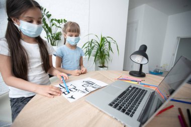 İnternette okuyan ve yüz maskesi takan iki küçük kız çocuğu..