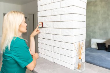 Kadın ısıyı evdeki beyaz duvara modern kablosuz termostatla düzenliyor. Akıllı ev ısıtma yönetmeliği kavramı.