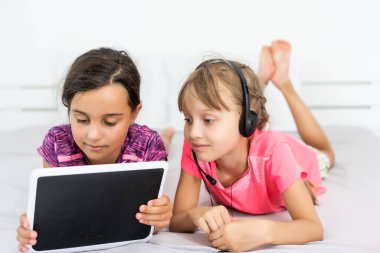 ev, eğlence, yeni teknoloji ve müzik konsepti - evde tablet bilgisayar ve kulaklıkla gülümseyen küçük kız.