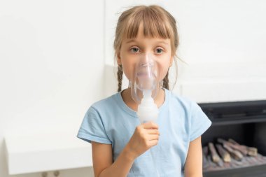 Küçük kız nebulizörle solunum yapıyor. Hasta çocuk solunum cihazını elinde tutuyor ve evde soluk alıp veriyor..