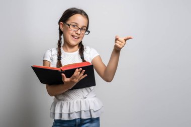 Ayakta duran ve beyaz arka planda kitap tutan sevimli küçük kız..