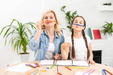 Anne ve kız güzel ve mutlu anneler günü için kağıt ve kalemlerle birlikte masaya oturarak bir kart yapın..