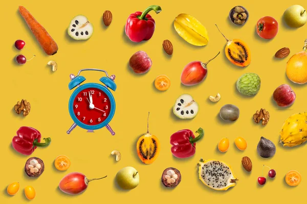 Healthy food concept, fruits and vegetables, carrots and green vegetables. alarm clock on yellow background.