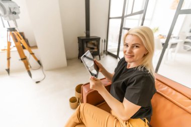 Kadın elleri ekranda akıllı ev sistemi olan bir tablet bilgisayarı tutuyor.