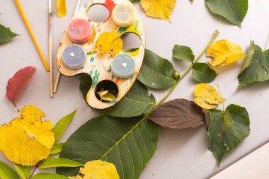 A child paints a picture of an autumn leaf with paints. Childrens hands. Favorite hobby, materials for creativity. High quality photo