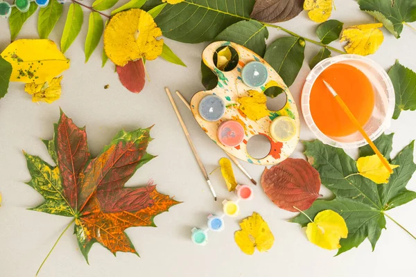 A child paints a picture of an autumn leaf with paints. Childrens hands. Favorite hobby, materials for creativity. High quality photo