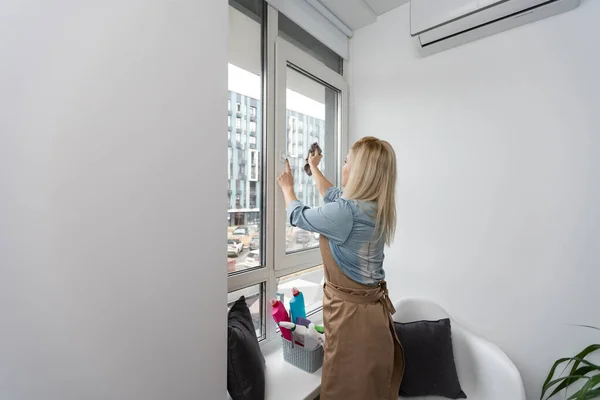 Housewife sprays the detergent on the window and wipes the window with a clean microfiber cloth. Clean transparent windows without streaks. Woman Cleaning House concept