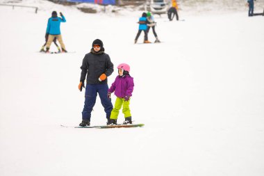 Eğitmenler kar yamacındaki bir çocuğa snowboard yapmayı öğretiyor.