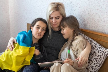 Savaşa karşı aileler. Anne ve iki kız yatakta Ukrayna bayrağıyla kitap okuyorlar.