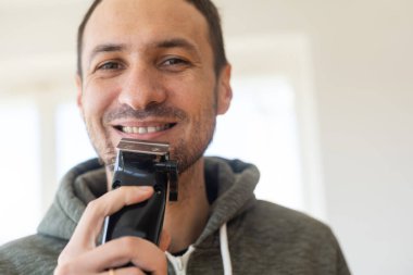 Yakışıklı genç adam gri arka plan üzerinde elektrikli ustura ile tıraş