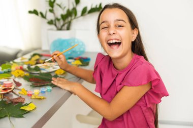 little girl artist with a brush and paints in her hands in autumn draws a landscape with leaves on canvas. High quality photo
