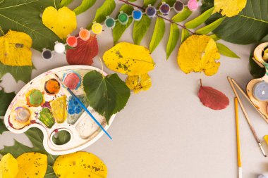 Girls paint patterns autumn leaf. Gouache, brush and various autumn leaves on a wooden table. Childrens art project. Colorful Hand-painted on dry autumn leaves. High quality photo