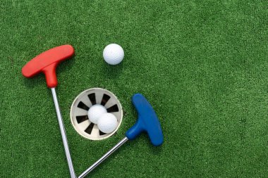 Assorted miniature golf putters and balls askew on synthetic grass