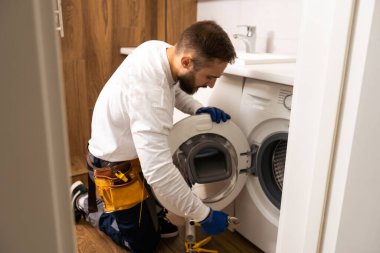 Usta bozuk çamaşır makinesini tamir ediyor..