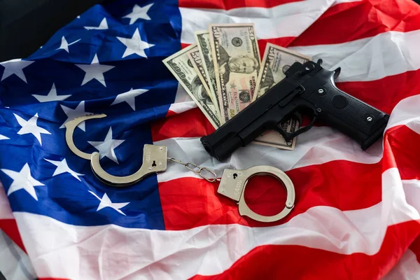 Gun, holster, handcuffs and cash in front of the American flag.