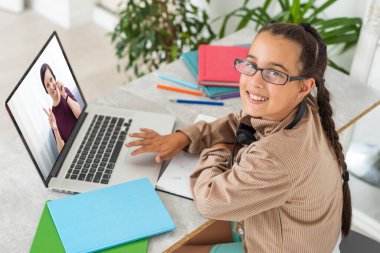 Portrait of little girl in wireless headset using laptop, studying online at home, interested happy student typing on keyboard looking at pc screen, watching webinar, online course, doing homework