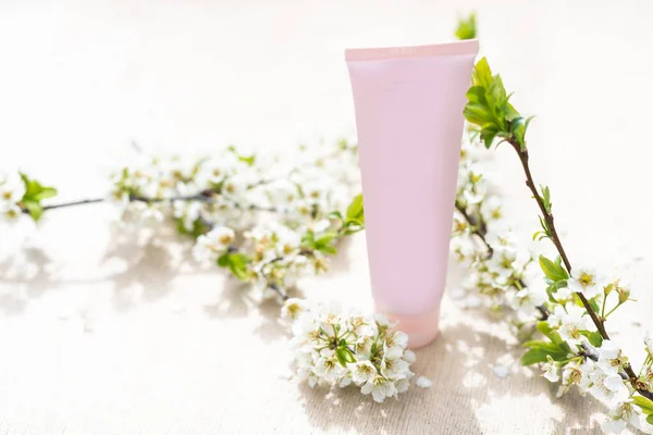 One white blank cosmetic tube bottle and flower, blooming branch on pink background. Natural Organic Spa Cosmetic Beauty Concept. Mockup Front view