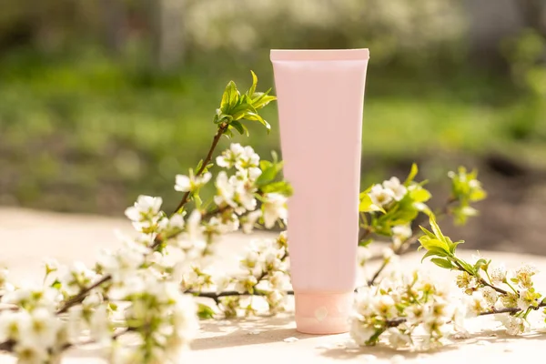 One white blank cosmetic tube bottle and flower, blooming branch on pink background. Natural Organic Spa Cosmetic Beauty Concept. Mockup Front view