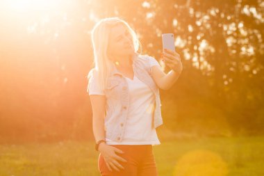 Çekici genç bir kadın, arka planda günbatımıyla parkta eğleniyor.