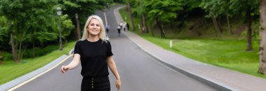 Günlük kıyafetlerle gezen neşeli genç bayan kırsal alanda asfalt yolda yürüyor, dışarıda otostop çekiyor. Güzel milenyum kadını otostop ile tek başına seyahat ediyor..