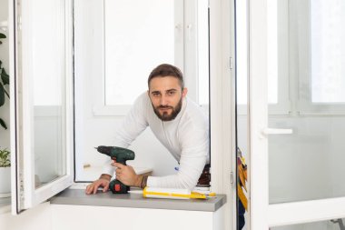 Yakışıklı genç adam yeni bir inşaat alanına pencere takıyor.