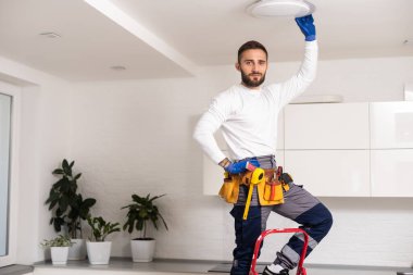 Elektrik işçisi yeni dairede lamba monte ediyor.