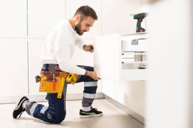 Genç adam mutfak mobilyalarını monte ediyor..