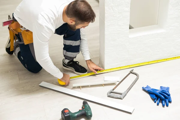 A man installs a floor skirting board. Fixing the plastic skirting board with screws to the wall. Home renovation