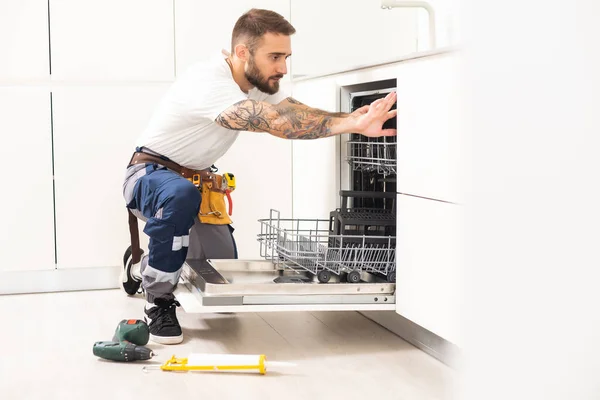 Technician or plumber repairing the dishwasher in a household.