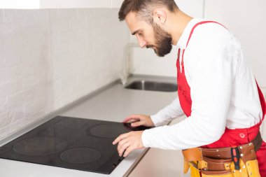 Adam mutfak yüzey dairesini elektrikle tamir ediyor. Tezgaha hob kuruluyor. Adam yeni mutfak mobilyaları ve aletler almış. Elektrikçi ev aletleri kurma işlemi