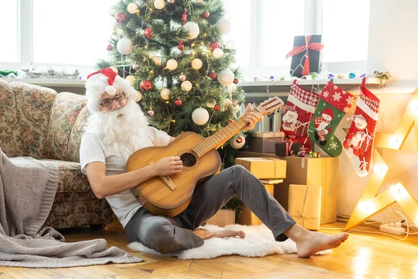 Bearded man in Santa costume with broken guitar. Musical instrument. Rock guitarist. New year. Christmas time.