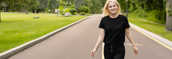 Радостная юная леди в повседневной одежде, идущая по асфальтовой дороге в сельской местности, автостопом на прогулку на открытом воздухе. Прекрасная женщина тысячелетия путешествует в одиночку на автостопе.