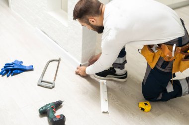 The craftsman measures the length of the plinth for cutting, installing the plinth on the corner of the wall, close-up installation.