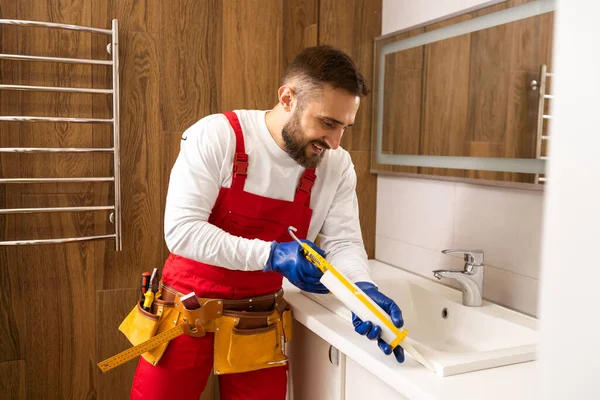 Profesyonel tesisatçı, üniformalı erkek işçi yeni daireye lavabo ve su borusu kuruyor..