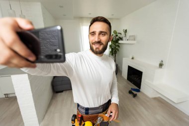 Gülümseyen yakışıklı inşaatçı cep telefonuyla selfie çekiyor..